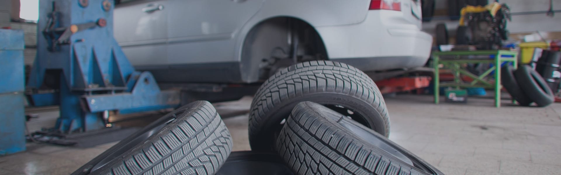 Car raised on a lift with spare tyres on the workshop floor